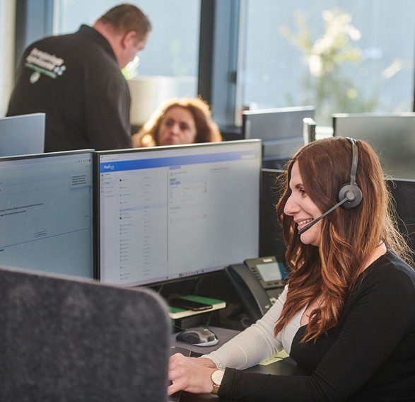 Kundeservicemedarbejder med headset arbejder ved sin computer i et moderne og dynamisk kontormiljø.