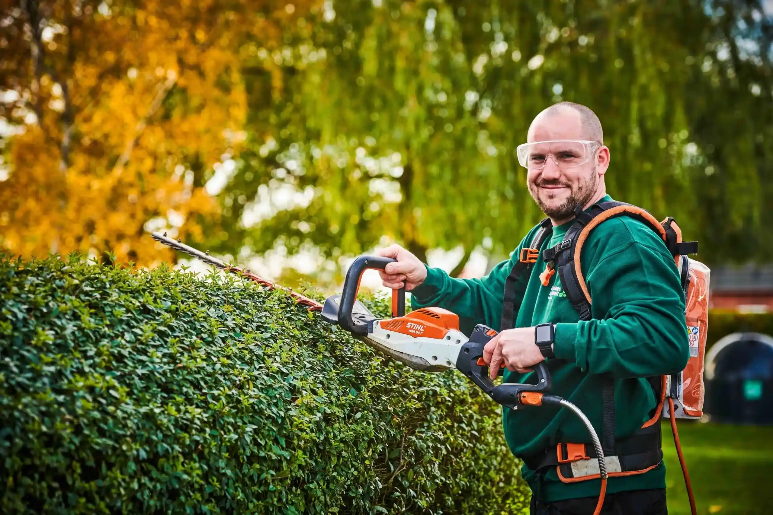 Medarbejder udfører hækklipning med elektrisk hækkeklipper og sikkerhedsudstyr