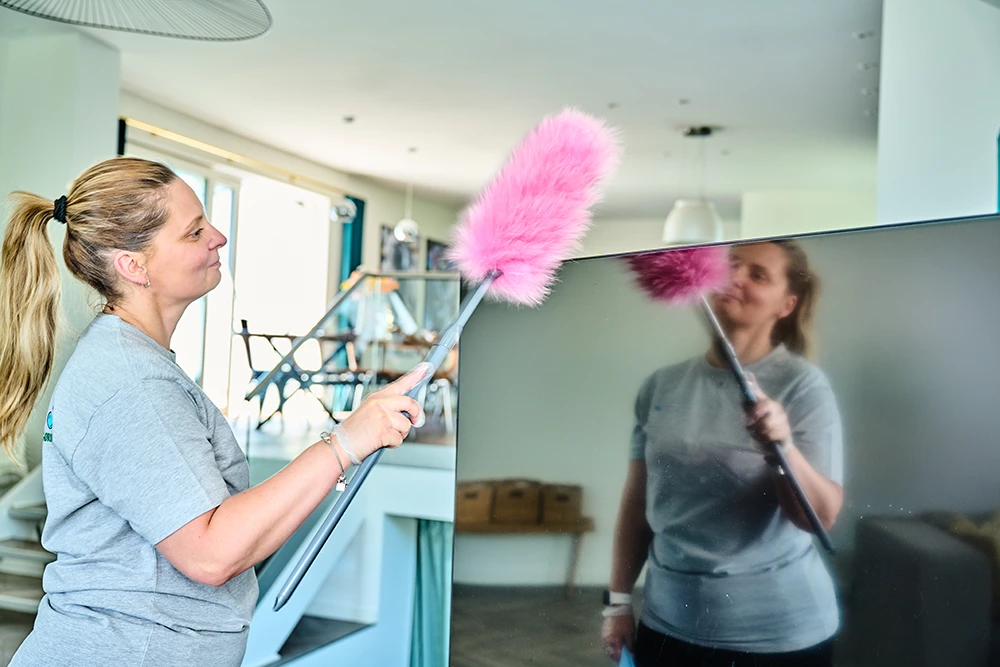 Medarbejder udfører privatrengøring og afstøver fladskærm med pink fjerkost.