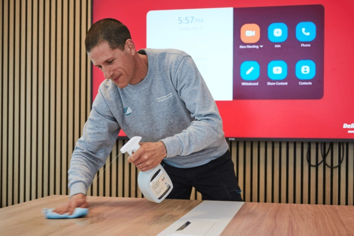 Mandlig medarbejder udfører erhvervsrengøring af kontorbord med svanemærket rengøringsmiddel