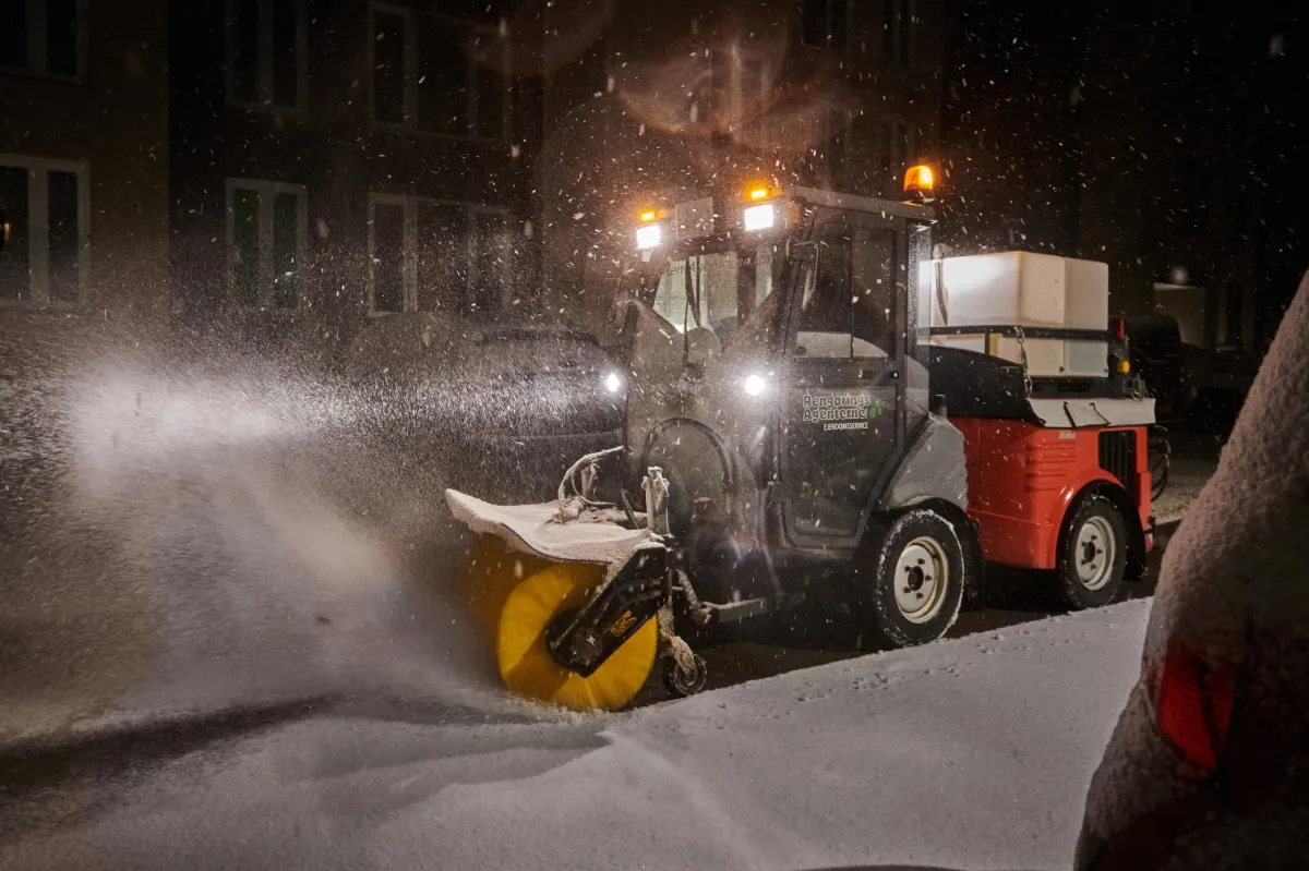 Snerydningsmaskine rydder sne i boligområde om natten med kraftigt lys og roterende kost.