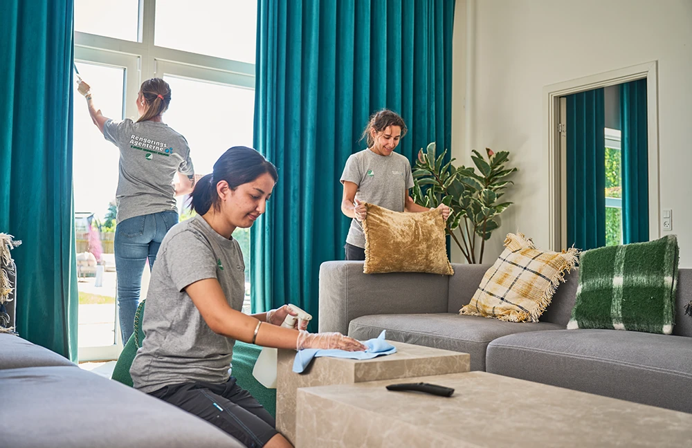 Tre medarbejdere udfører privatrengøring i stue med vinduespudsning og pudearbejde.